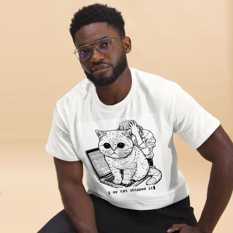 Man wearing a white tee printed with a grumpy cat sitting on a laptop and the line “$ my cat shipped it”